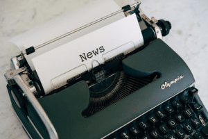 ​​Typed on a piece of paper it says "News" inside an old Olympia typewriter placed on a marble table.